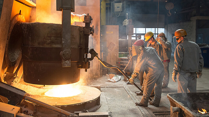 Arbeiter stehen vor einem Stahlkessel mit flüssigem Metall